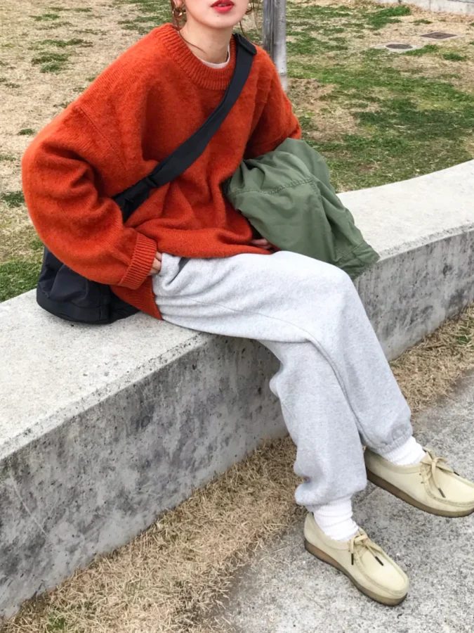 赤いセーターとグレーのパンツを着た人物が公園のベンチに座っているファッションスタイル。